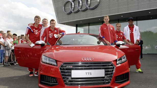 Mehrere Fußballspieler des FC Bayern München posieren vor einem roten Audi TTS.