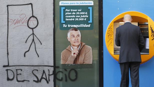 Ein Mann benutzt einen Geldautomaten neben Graffiti und einem Werbeplakat.