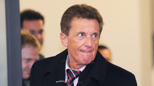 Ein Mann mit dunkler Jacke und Krawatte blickt zur Seite.