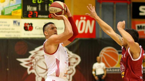Ein Basketballspieler zielt auf den Korb, während ein Gegenspieler ihn zu blocken versucht.