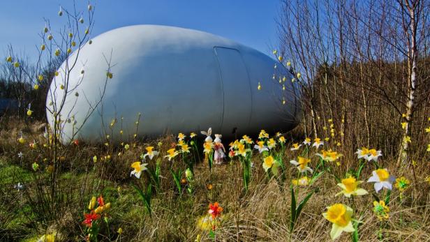 Ein großes, weißes Gebäude steht inmitten einer Wiese mit Narzissen und Osterdekorationen.