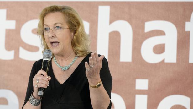 Eine Frau mit Brille spricht in ein Mikrofon vor einem Schriftzug.