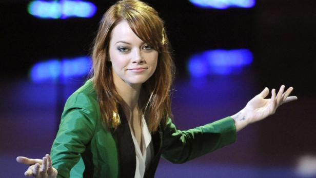 Emma Stone in einer grünen Jacke gestikuliert auf einer Bühne.
