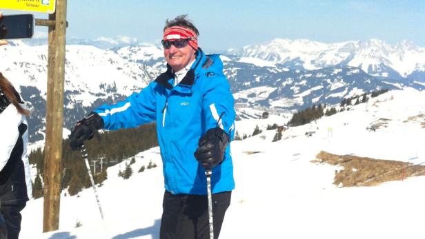 Ein Mann mit Skiausrüstung steht vor einer verschneiten Berglandschaft.