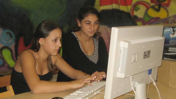 Zwei junge Frauen sitzen vor einem Computer und tippen auf der Tastatur.