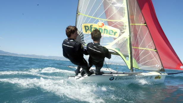 Zwei Segler steuern ein kleines Segelboot mit „Pfanner“-Werbung auf dem Meer.
