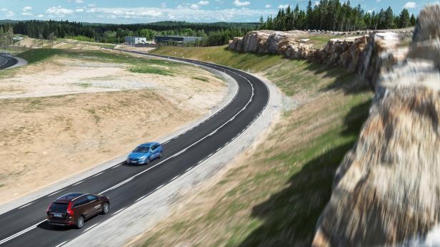 Zwei Autos fahren auf einer kurvenreichen Straße durch eine hügelige Landschaft.
