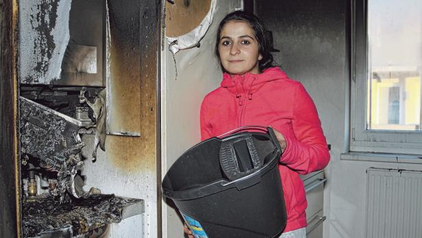Eine junge Frau steht mit einem Putzeimer in einer durch einen Brand beschädigten Küche.