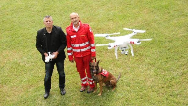 Axel Jungwirth (links) und Johann Katzgraber vom Roten Kreuz beobachten gemeinsam mit Suchhund Cliff eine fliegende Drohne. Sie soll spätestens im nächsten Jahr zum Einsatz kommen.