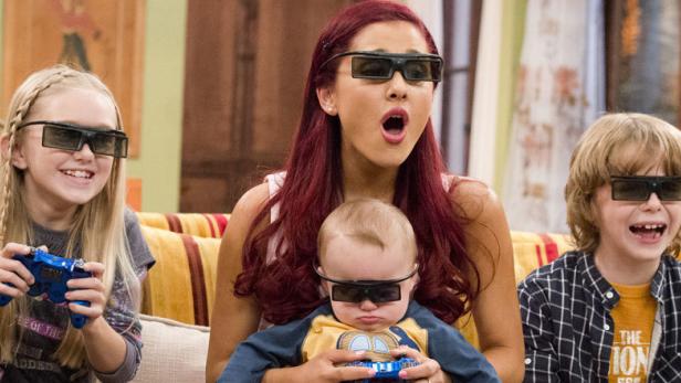 Eine Frau mit roten Haaren und drei Kinder sitzen auf einem Sofa und tragen 3D-Brillen.