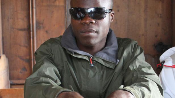 Ein Mann mit Sonnenbrille sitzt an einem Holztisch.