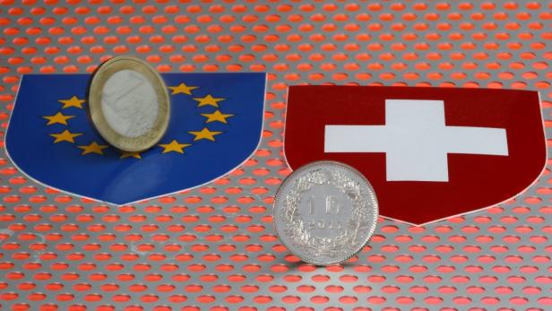 Eine Euro-Münze vor der EU-Flagge und ein Schweizer Franken vor der Schweizer Flagge.
