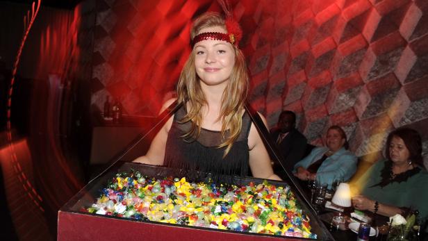 Eine Frau im Charleston-Stil präsentiert Süßigkeiten auf einem Tablett.