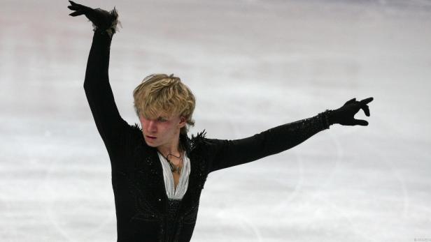 Ein Eiskunstläufer in einem schwarzen Kostüm präsentiert eine ausdrucksstarke Pose auf dem Eis.