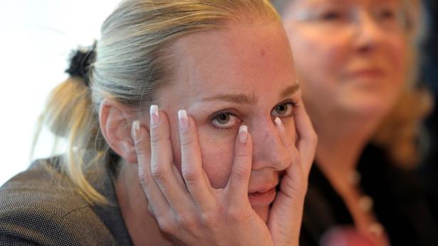 Eine Frau mit blonden Haaren blickt mit ihren Händen vor dem Gesicht zur Seite.