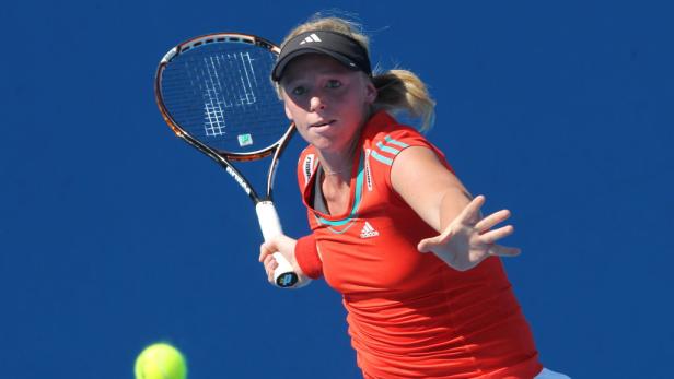 Eine Tennisspielerin schlägt einen Ball vor einem blauen Hintergrund.