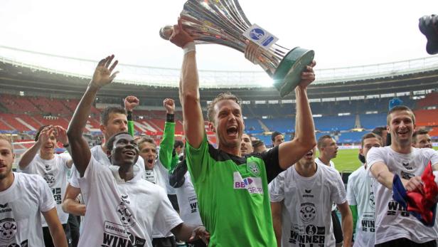 Eine Fußballmannschaft feiert mit dem Pokal in einem Stadion.
