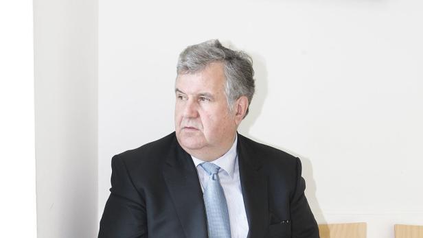 Ein Mann mit grauem Haar, Anzug und Krawatte blickt zur Seite.