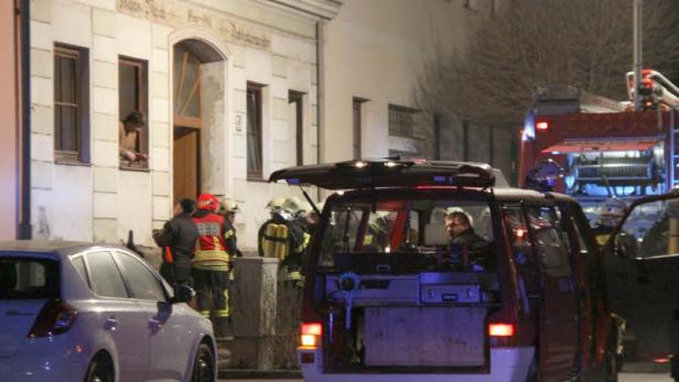 Feuerwehrleute stehen vor einem Gebäude, während eine Person aus einem Fenster schaut.