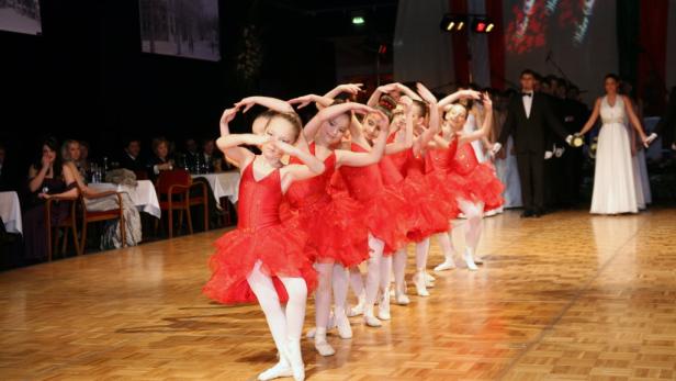 Eine Gruppe junger Tänzerinnen in roten Tutus führt eine Choreografie auf einer Bühne auf.