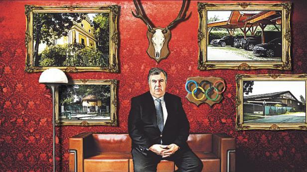 Ein Mann sitzt auf einem Sofa vor einer Wand mit Bildern von Häusern, Autos und olympischen Ringen.