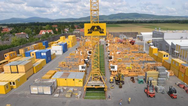 Ein Lagerplatz mit vielen gelben Containern und zerlegten Kränen der Firma Alpine.