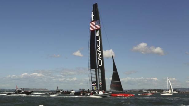 Ein Segelboot mit dem Schriftzug „Oracle“ und der amerikanischen Flagge auf dem Mast fährt auf dem Wasser.