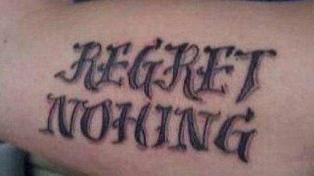 Ein Tattoo auf einem Arm zeigt den Schriftzug „Regret Nothing“.