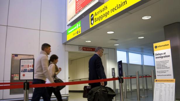 Reisende passieren die Gepäckausgabe in einem Flughafen.