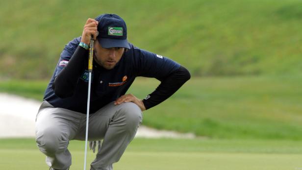 Ein Golfspieler kauert auf dem Grün und zielt mit seinem Putter.