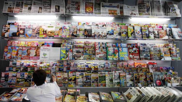 Eine Person steht vor einem Regal voller Zeitungen und Zeitschriften.