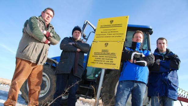 Vier Männer stehen vor einem Traktor und einem Schild, das auf ein militärisches Sperrgebiet hinweist.