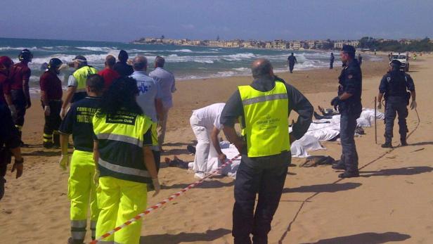 Rettungskräfte und Polizei am Strand nach einem Unglück, im Hintergrund eine Stadt.