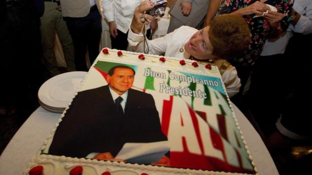 Eine Frau fotografiert eine Geburtstagstorte mit dem Bild von Silvio Berlusconi.