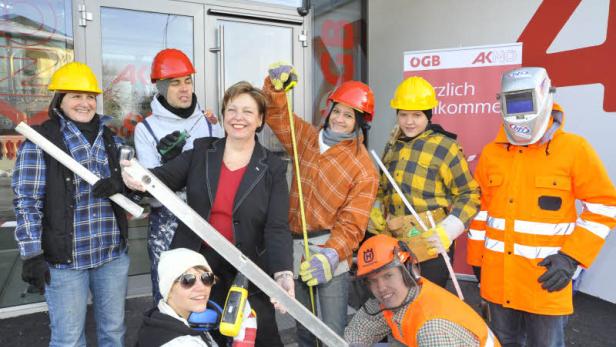 Eine Gruppe von Bauarbeitern und eine Frau im Blazer posieren vor einem Gebäude.