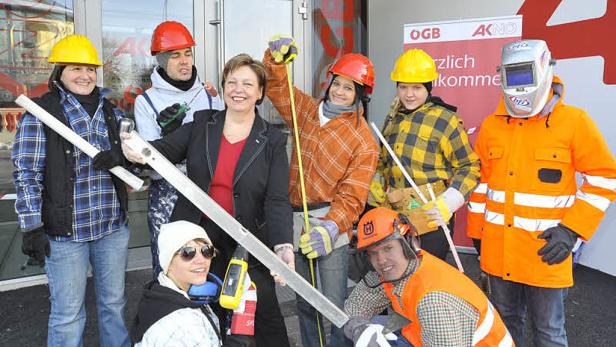Eine Gruppe von Bauarbeitern posiert mit Werkzeugen vor einem Gebäude.