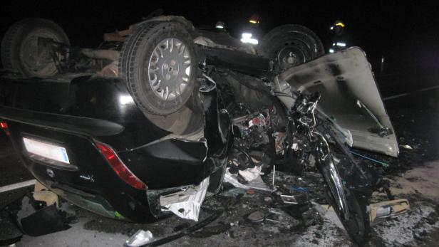 Ein schwarzes Auto liegt nach einem Unfall auf dem Dach, Rettungskräfte sind vor Ort.