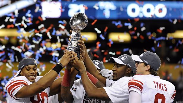 Spieler der New York Giants feiern mit der Vince Lombardi Trophy unter Konfettiregen.