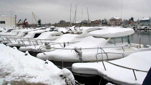 Einige mit Schnee bedeckte Boote liegen in einem Hafen.
