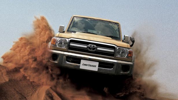 Ein goldfarbener Toyota Land Cruiser fährt durch eine Sanddüne.