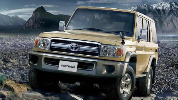 Ein goldfarbener Toyota Land Cruiser steht auf einem steinigen Untergrund vor einer Bergkulisse.