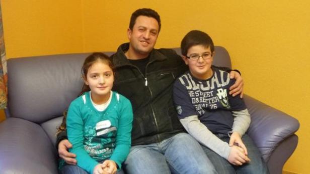 Ein Mann sitzt mit einem Mädchen und einem Jungen auf einem Sofa.