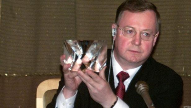 Ein Mann im Anzug präsentiert einen Kristallglas-Pokal.