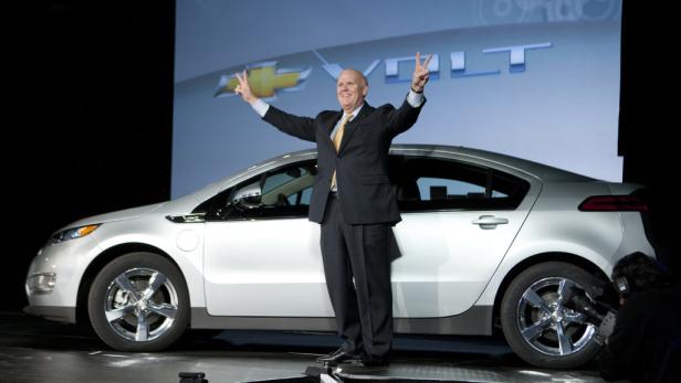 Ein Mann in einem Anzug posiert vor einem silbernen Chevrolet Volt.