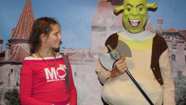 Ein Mädchen und eine als Shrek verkleidete Person posieren vor einem Schloss.
