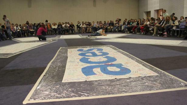 Eine Gruppe von Menschen sitzt um große Banner mit Unterschriften.