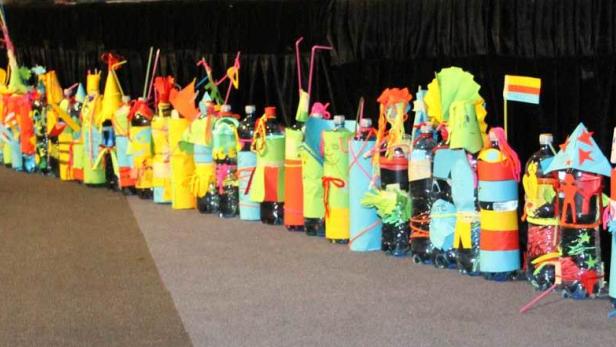 Eine Reihe bunter, dekorierter Plastikflaschen steht auf einem Teppich.