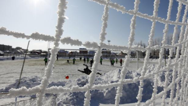 Ein Fußballspiel findet im Schnee statt, gesehen durch ein vereistes Tornetz.