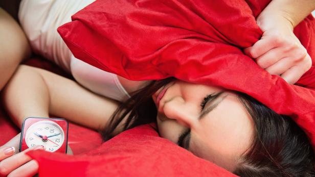 sleeping young woman in bed closes her ears with pillow