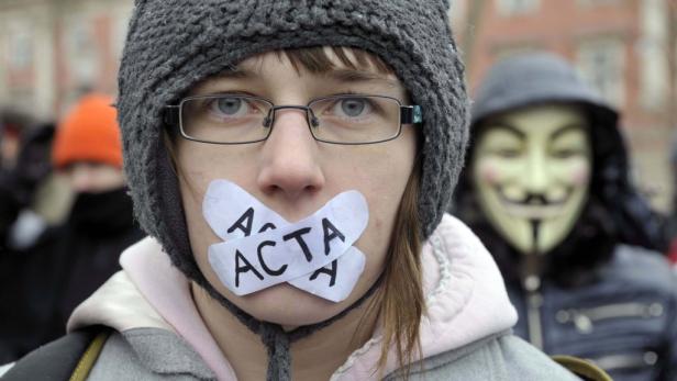 Eine Demonstrantin mit einem „ACTA“-Aufkleber über dem Mund, im Hintergrund eine Person mit Guy-Fawkes-Maske.